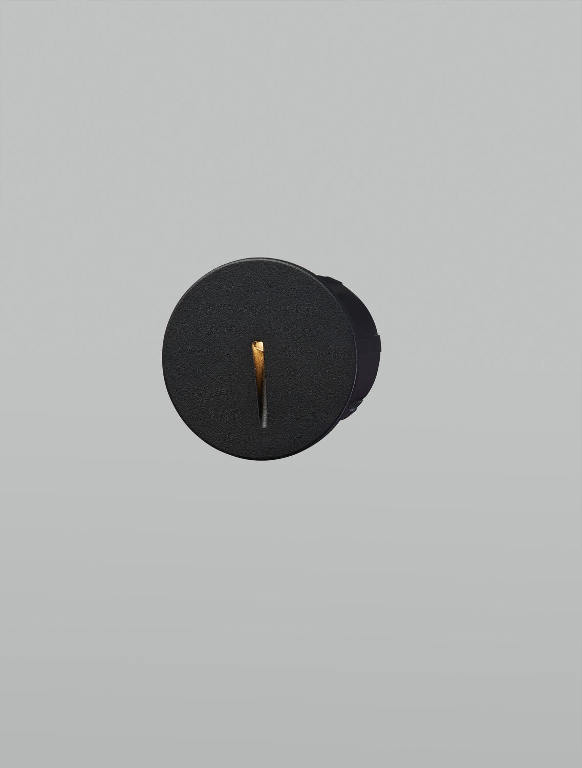 Applique noire allumée, la fente verticale diffuse une lumière chaude dorée.