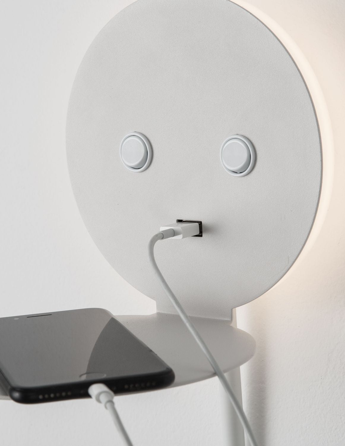 Gros plan sur une applique murale blanche avec téléphone en charge et port USB.