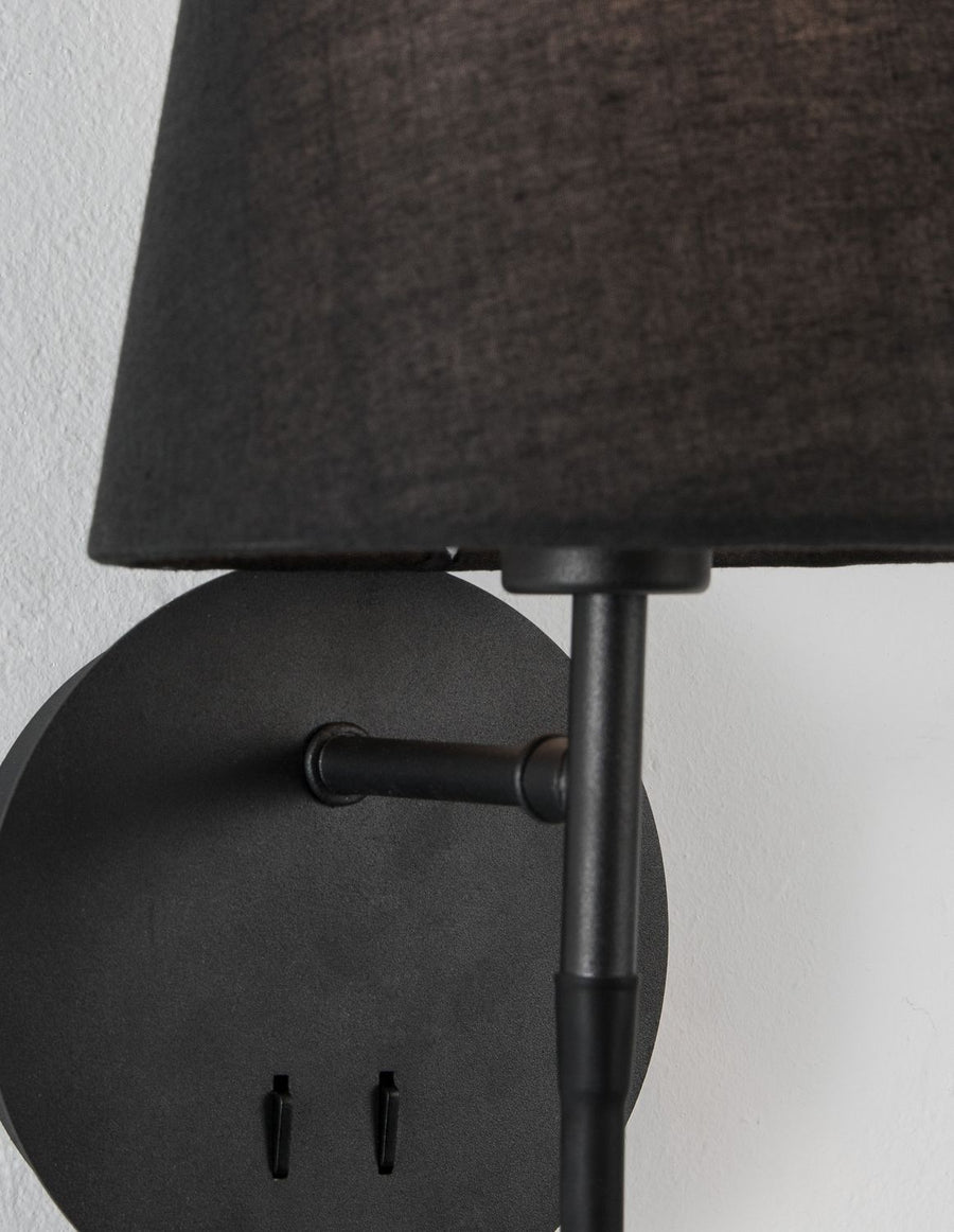 Détail du socle rond, du bras métallique et de l'abat-jour en tissu noir.
