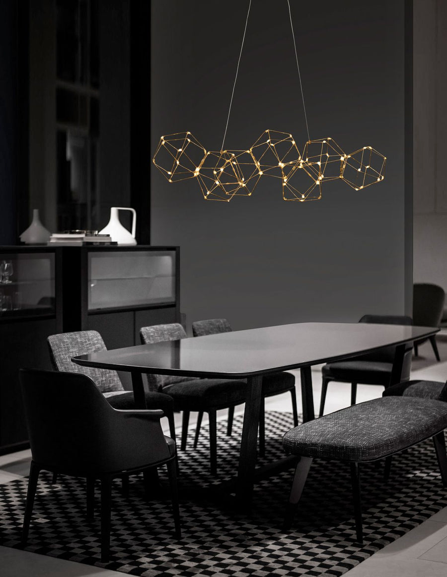 Suspension dorée géométrique suspendue au-dessus d'une table de salle à manger sombre