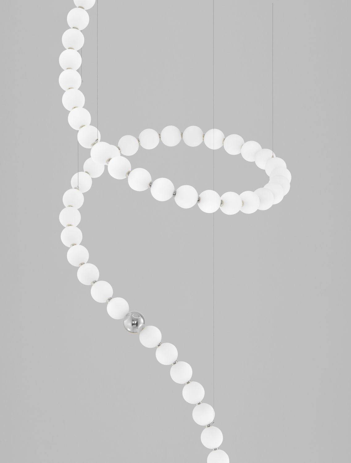 Gros plan sur les sphères de verre opalin et l'anneau chromé reliant le câble