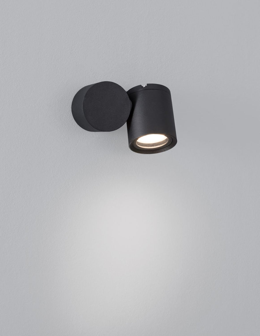 Applique allumée projetant un halo lumineux diffus sur le mur gris