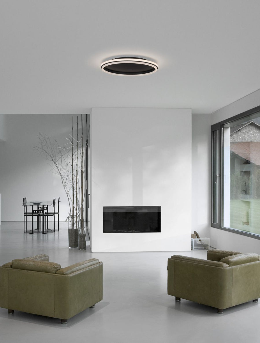 Plafonnier rond noir installé au plafond d'un salon moderne minimaliste tout en blanc