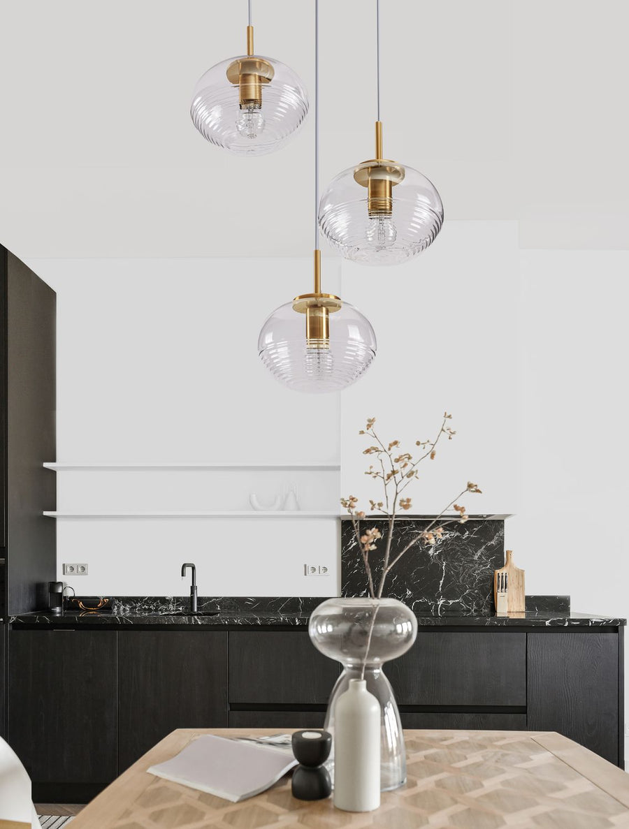 Suspension dorée à trois globes de verre allumés au-dessus d'une table de cuisine
