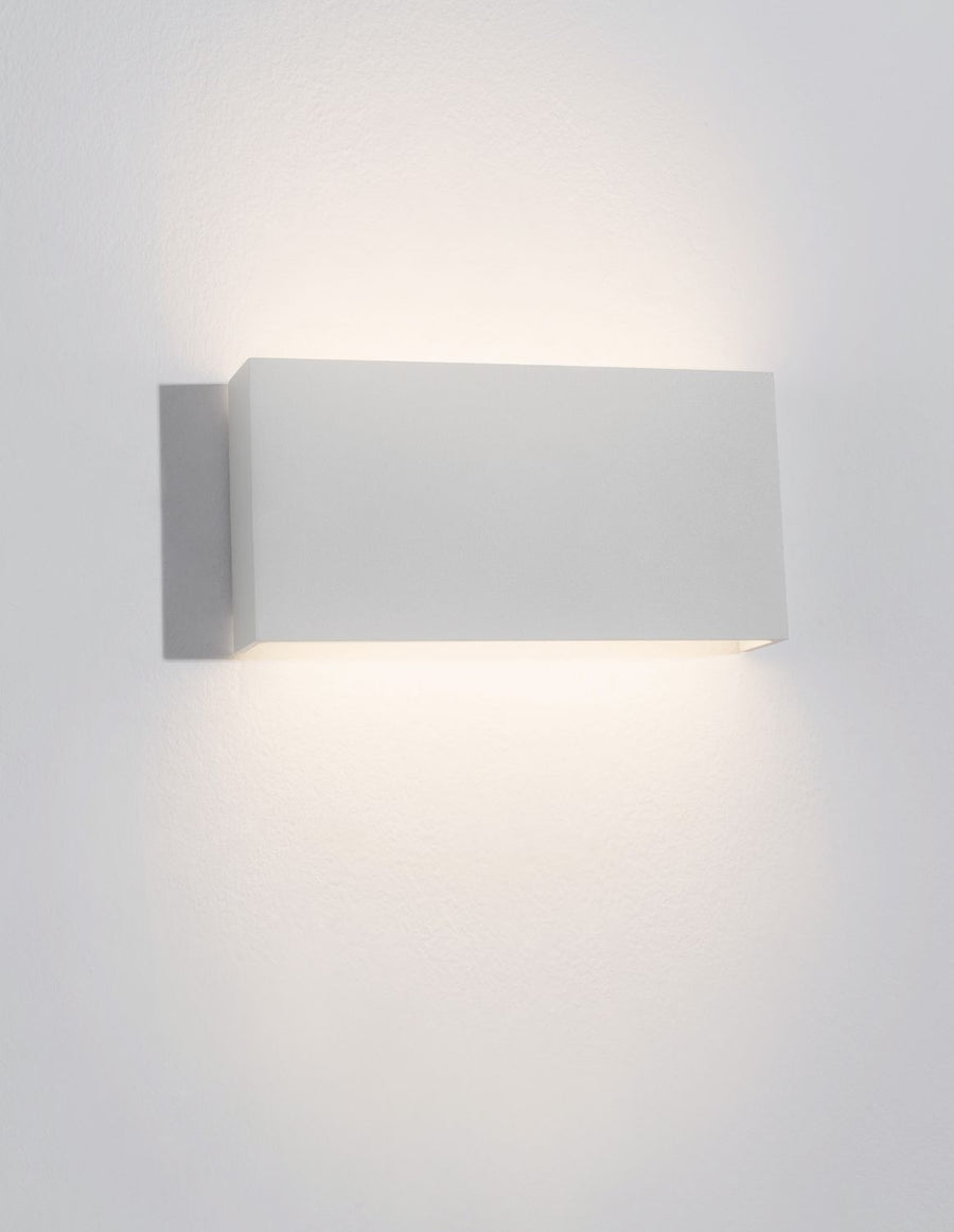 Luminaire allumé diffusant un halo de lumière chaude vers le bas sur le mur