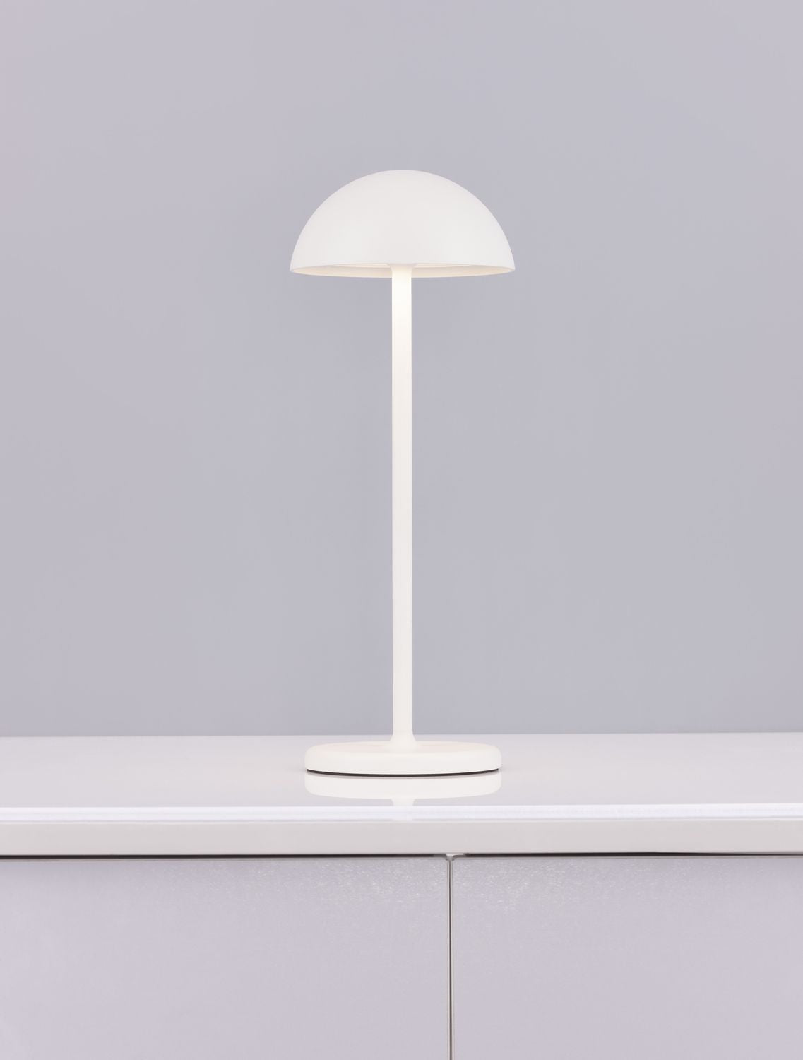 Lampe nomade blanche sur plan de travail gris, reflet sur la surface