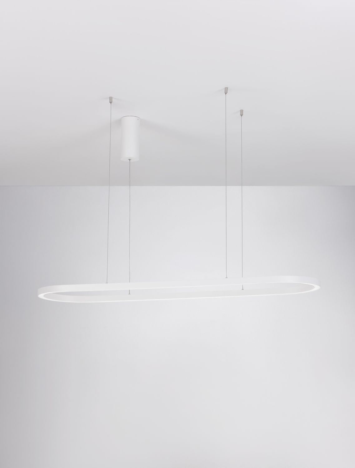 Vue de dessous de la suspension ovale allumée, câbles fins et fixation au plafond.