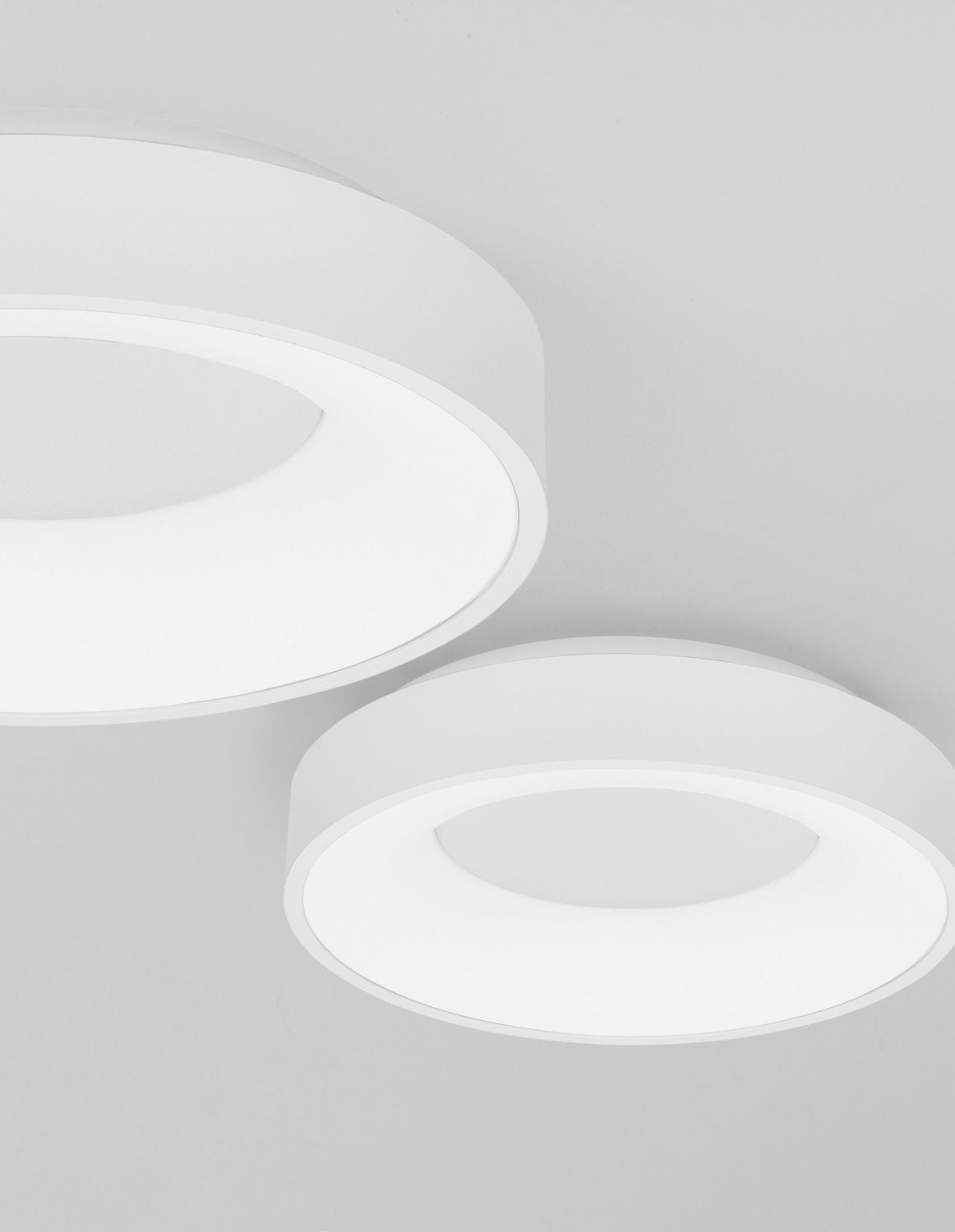 Deux plafonniers ronds blancs vus en angle sous un plafond neutre