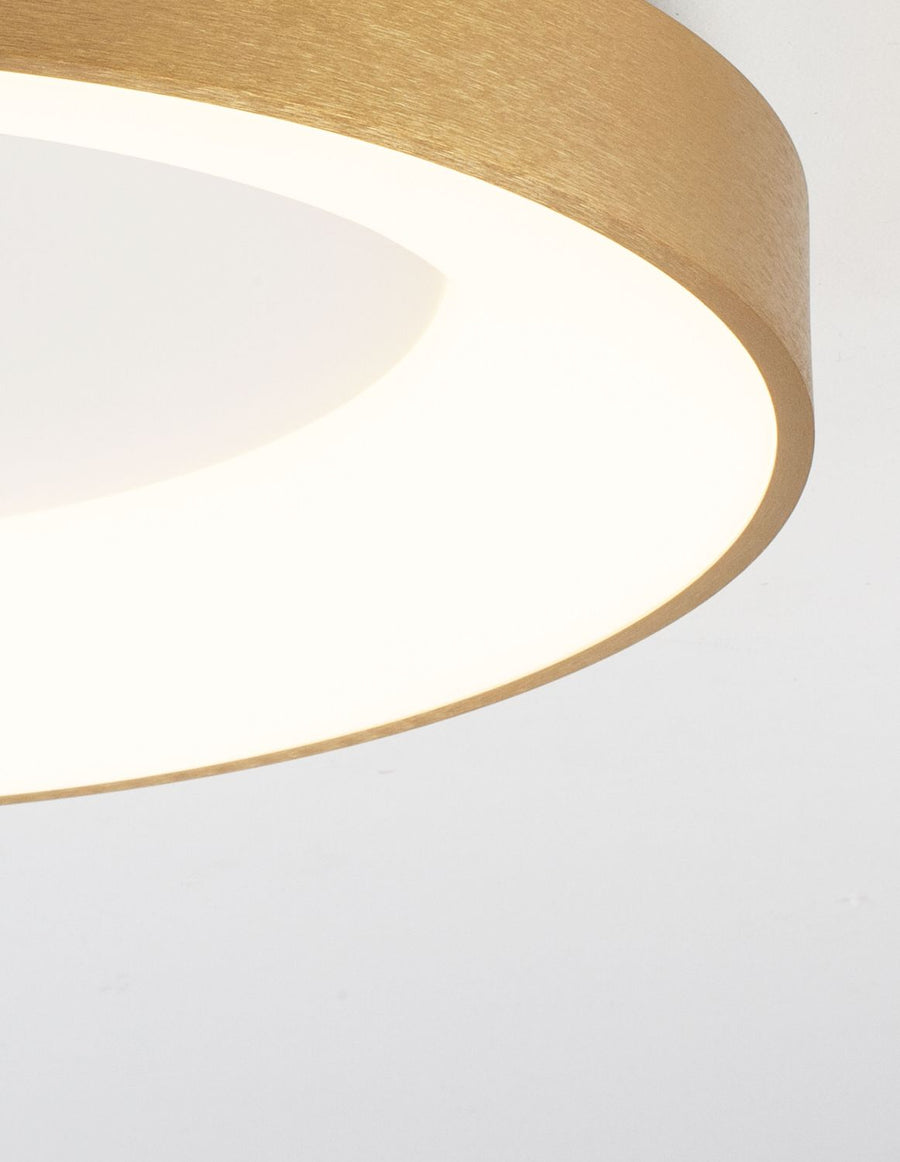 Détail de la tranche dorée brossée et du halo lumineux blanc sur plafond clair