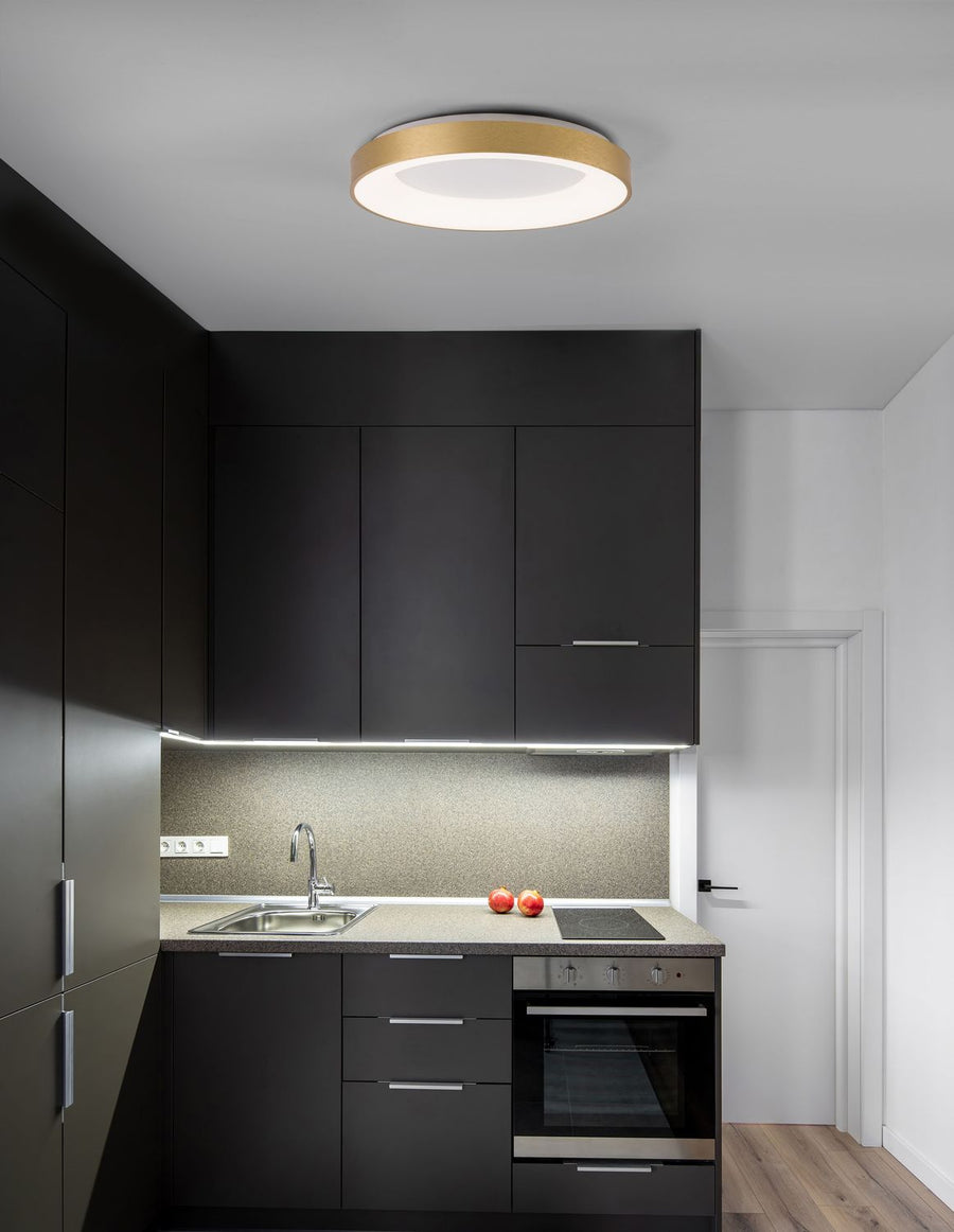 Plafonnier doré circulaire allumé au plafond d'une cuisine sombre moderne