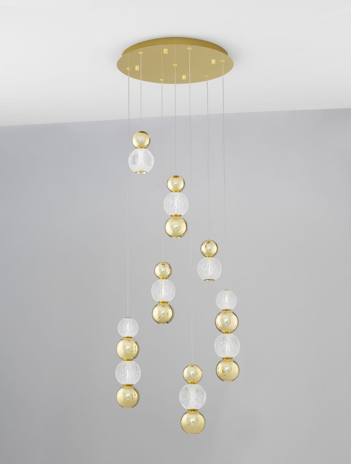 Suspension présentée sur fond gris clair, câbles fins et boules de verre dorées