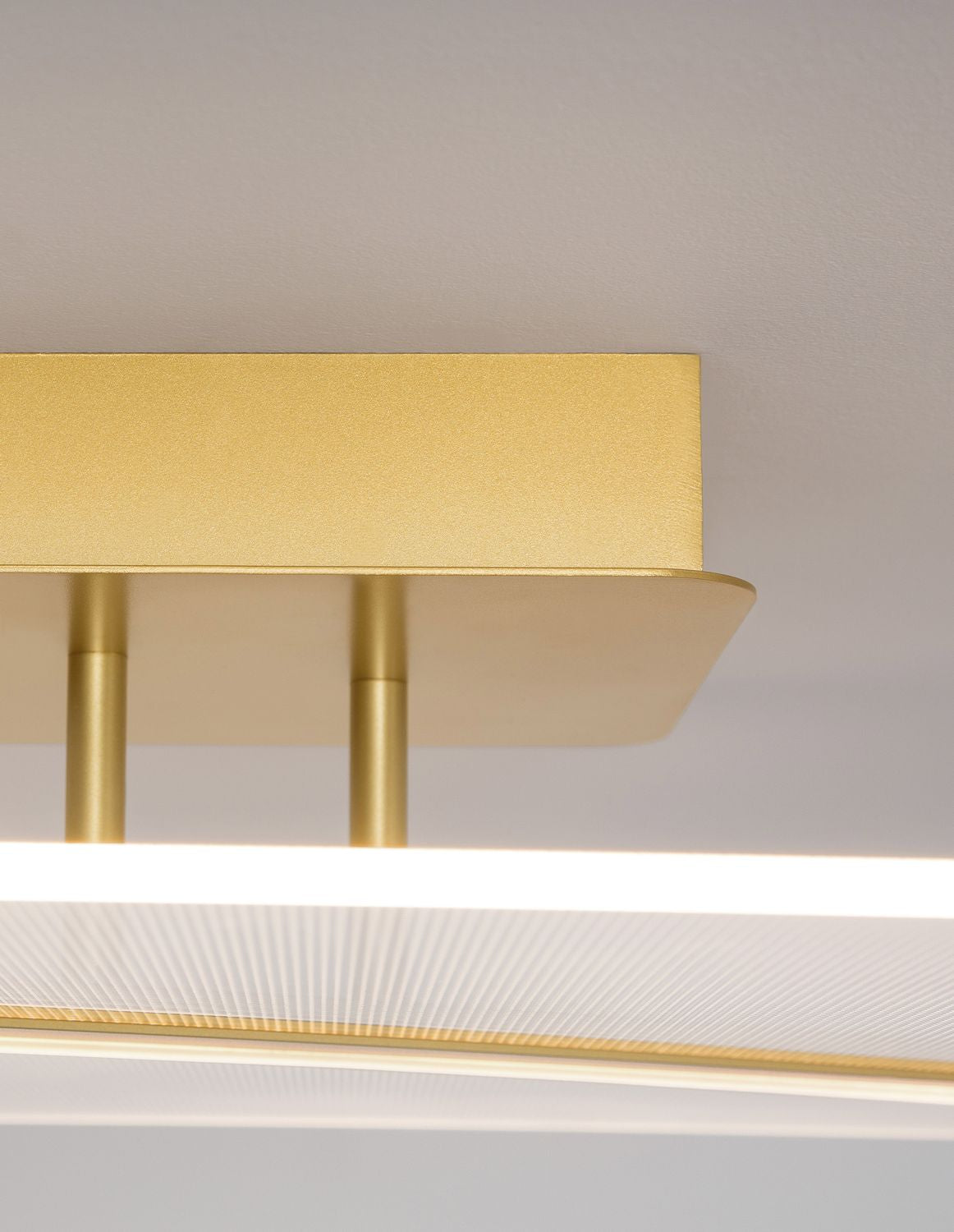Détail de la finition dorée et des tiges de fixation du plafonnier sous la lumière