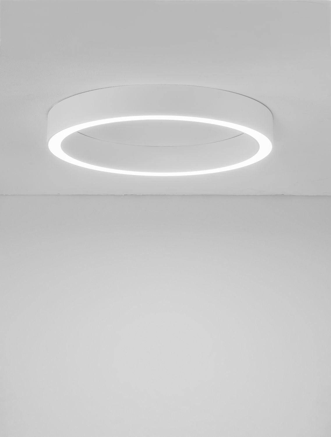 Plafonnier blanc installé au plafond, éclairé, avec ligne de jonction du mur visible.