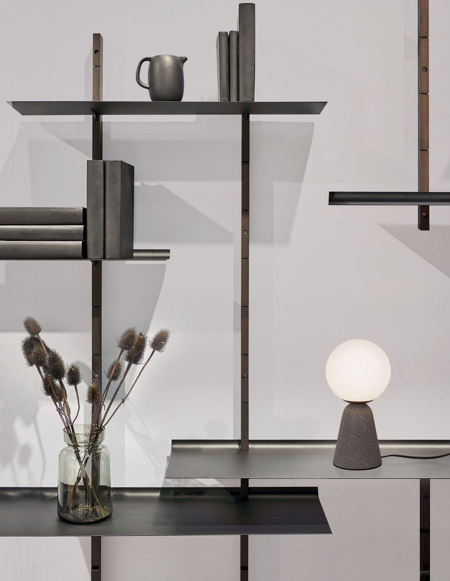 Lampe allumée posée sur une étagère en métal gris, décor de vase et de livres