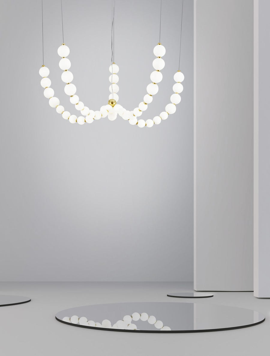 Suspension dorée en perles de verre blanc dans une pièce claire avec reflet