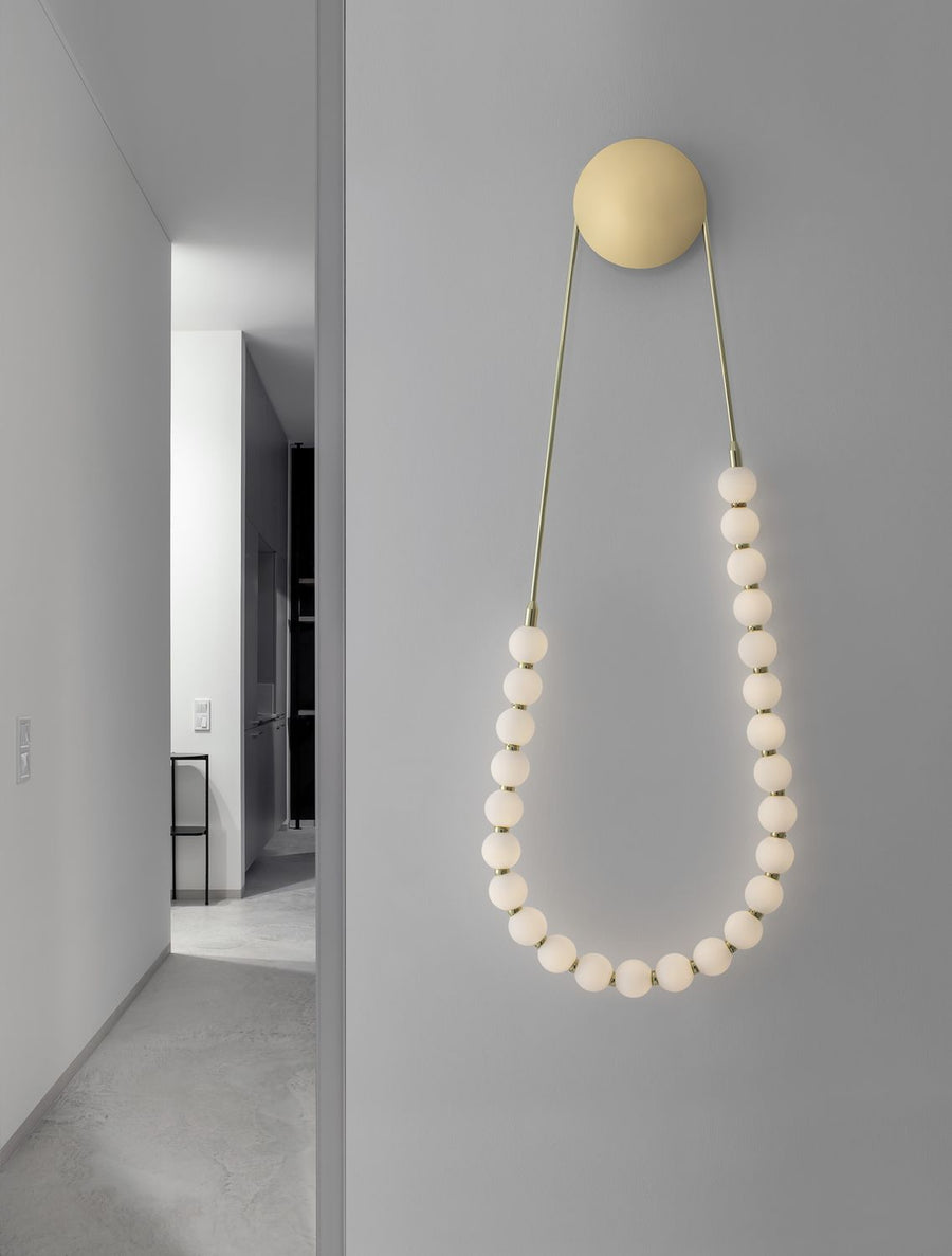 Applique murale dorée à chapelet de billes de verre blanches dans un couloir gris minimaliste