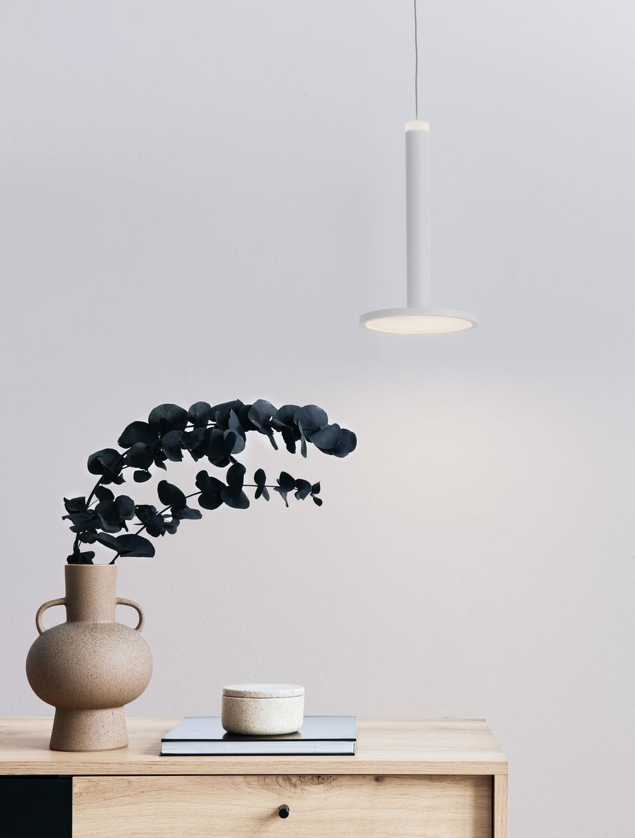 Suspension blanche allumée au-dessus d'un meuble en bois clair avec vase et eucalyptus