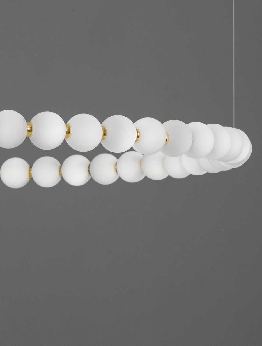 Détail rapproché des perles de verre blanc reliées par de fines bagues dorées