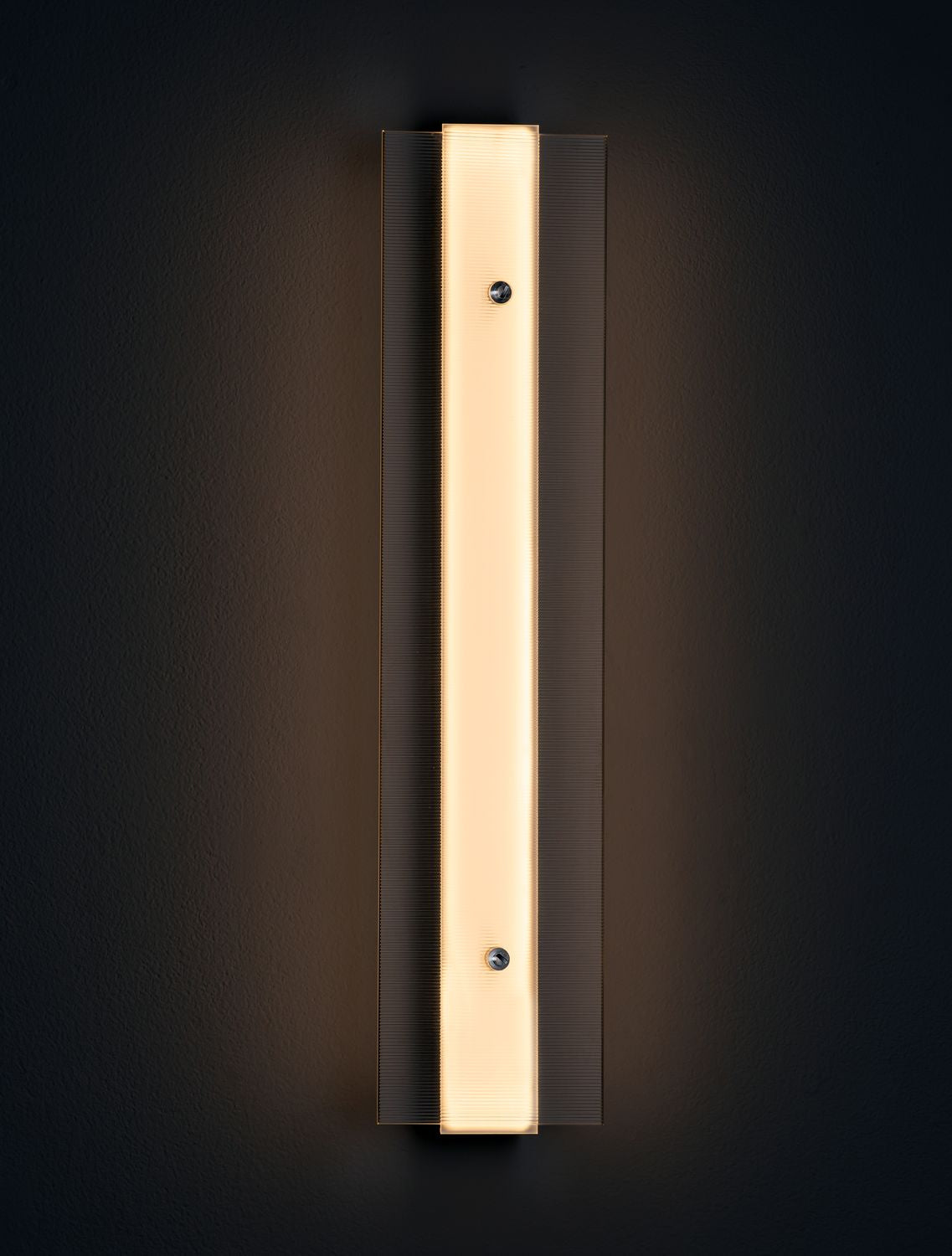 Mise en ambiance sur mur sombre, éclairage chaud soulignant le verre strié.