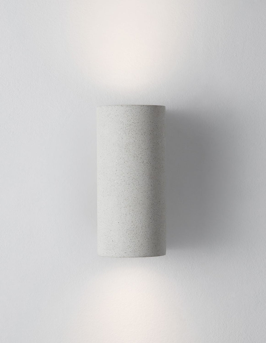 Applique murale allumée de face sur mur gris, halo lumineux diffus
