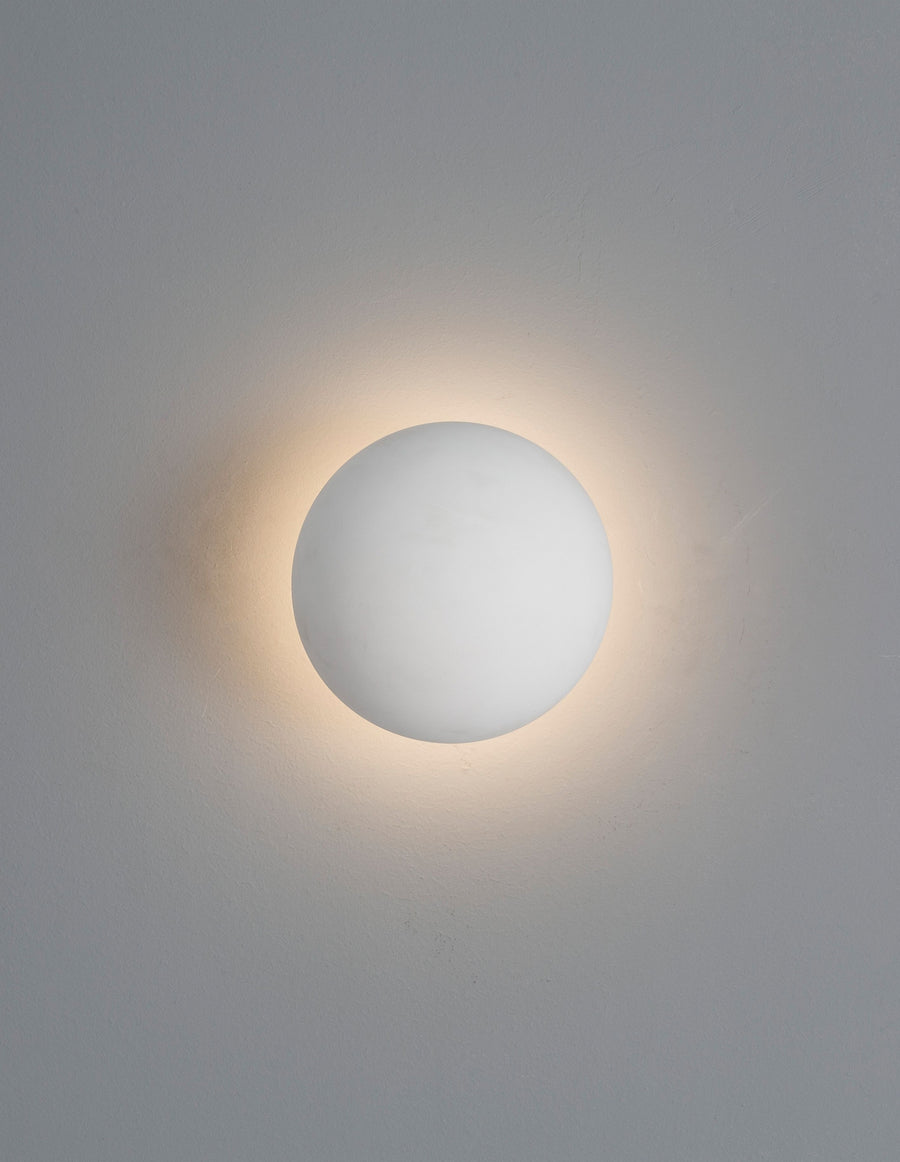 Applique murale sphérique blanche allumée, halo lumineux diffusé sur le mur gris