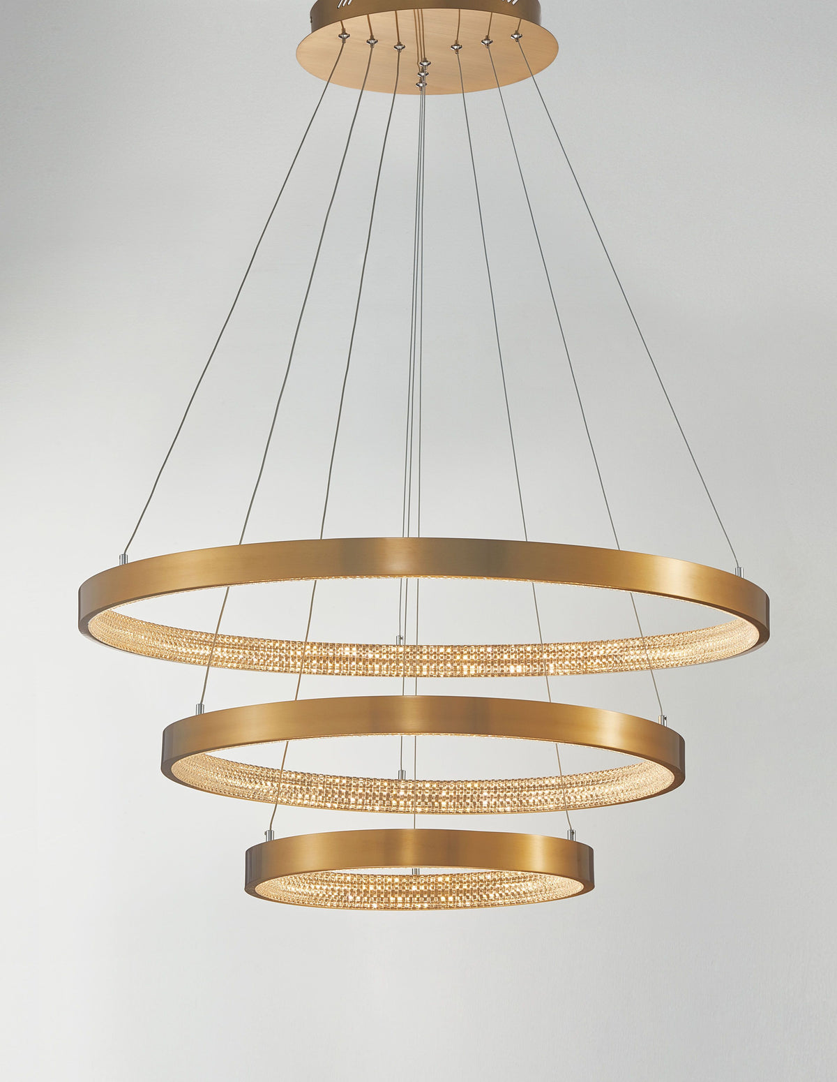 Vue de face du luminaire allumé, anneaux dorés diffusant une lumière chaude et scintillante