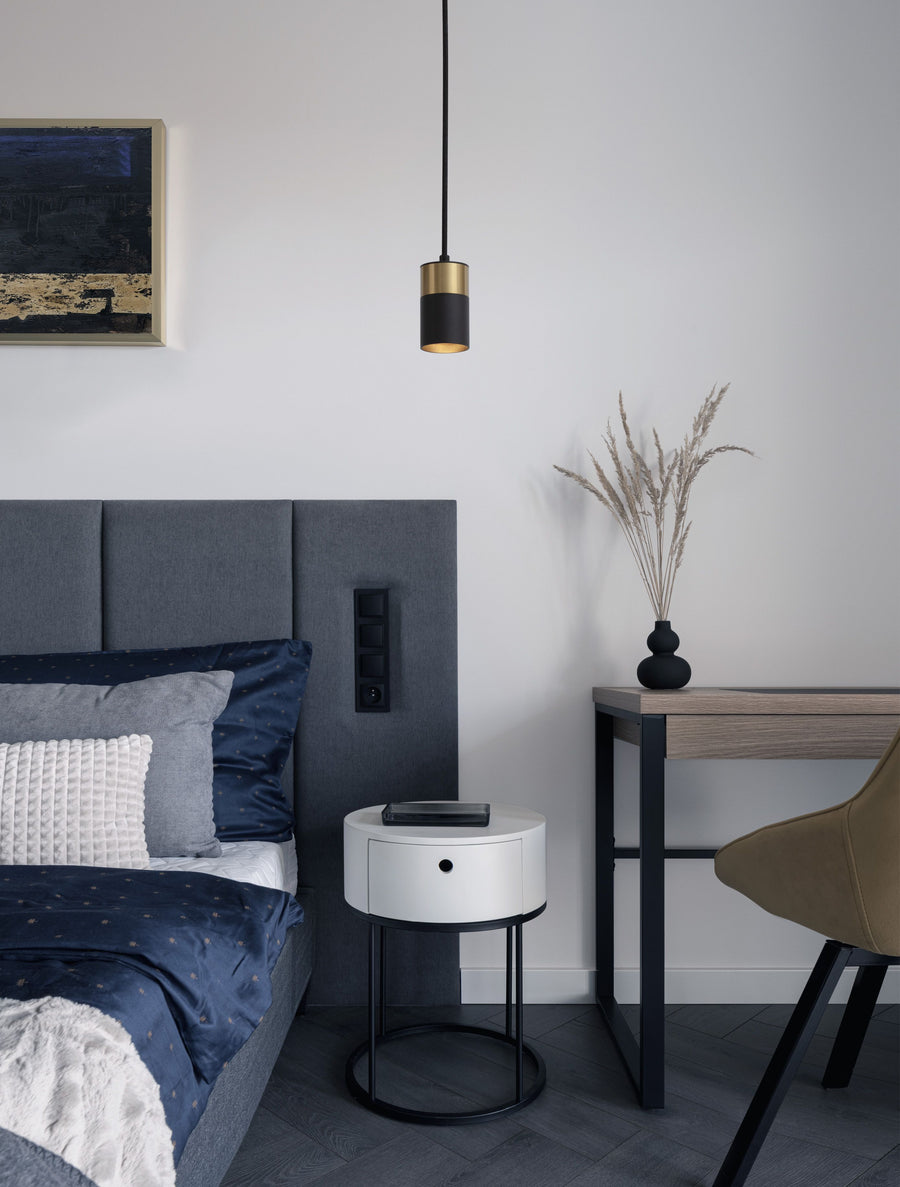 Suspension noire et dorée éclairant une chambre, au-dessus d'une table de chevet blanche