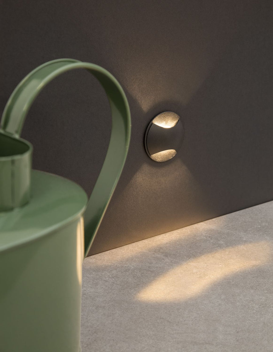 Applique murale noire ronde diffusant un halo lumineux haut et bas sur un mur sombre