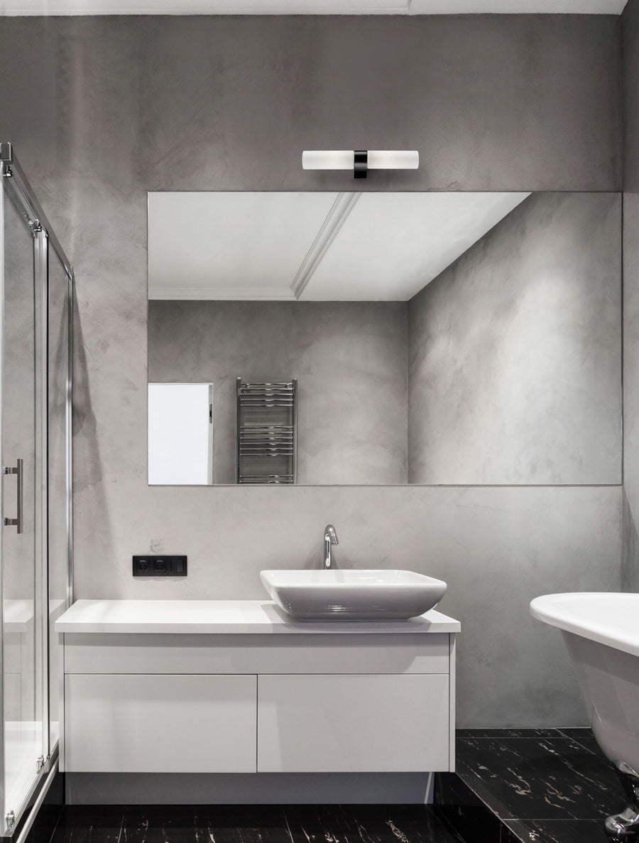 Applique murale noire allumée au-dessus d'un miroir de salle de bain grise