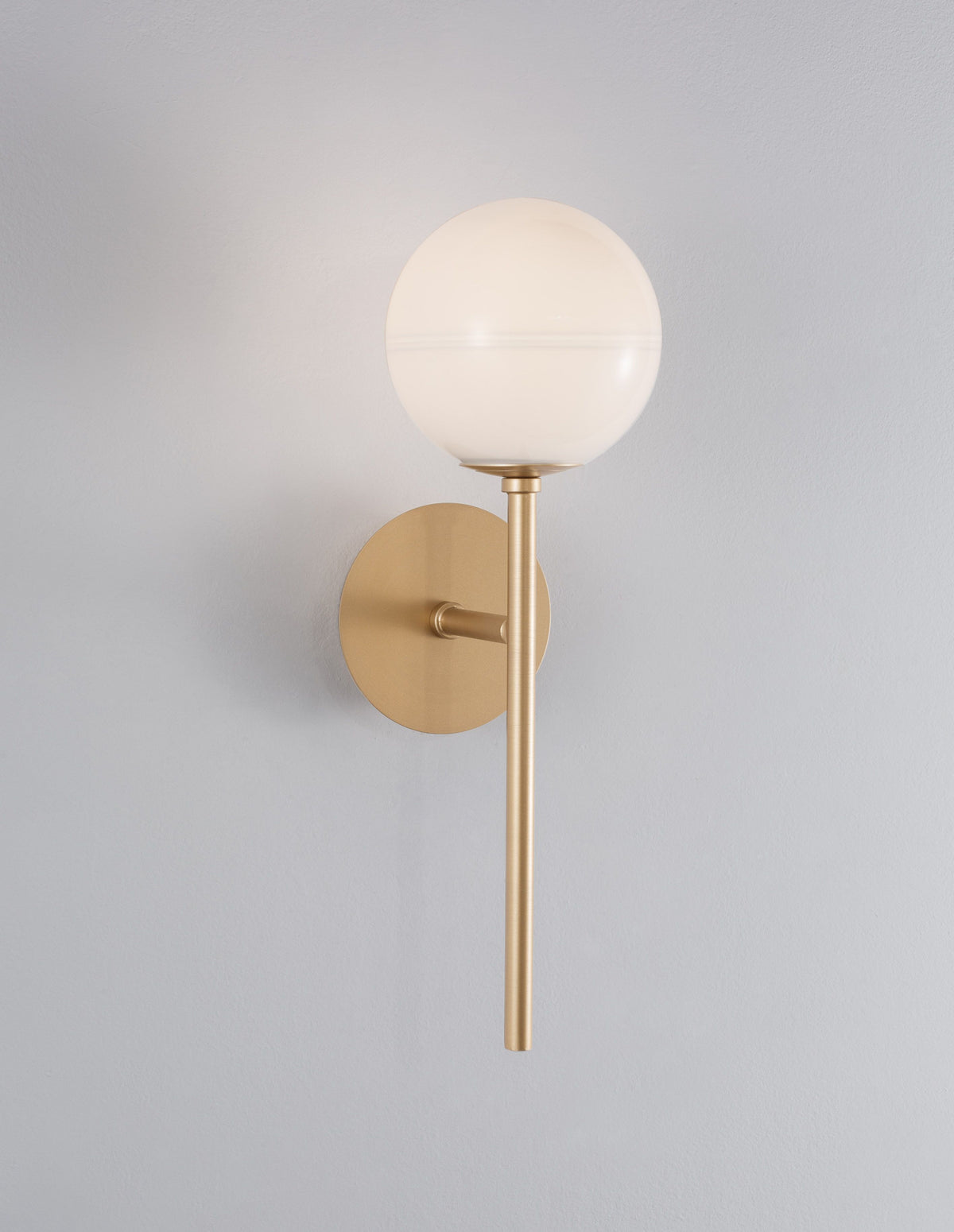 Gros plan de l'applique dorée sur mur gris, globe en verre blanc allumé