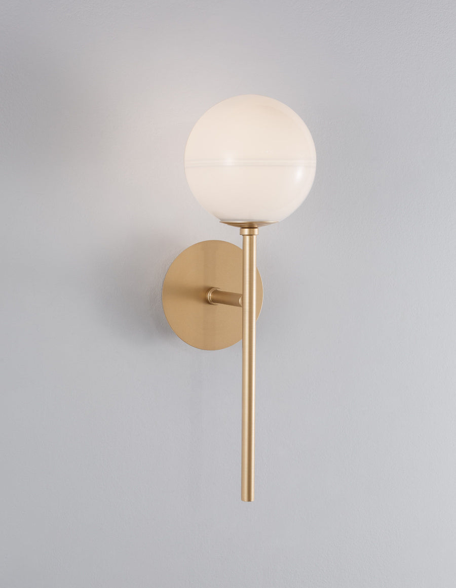 Gros plan de l'applique dorée sur mur gris, globe en verre blanc allumé