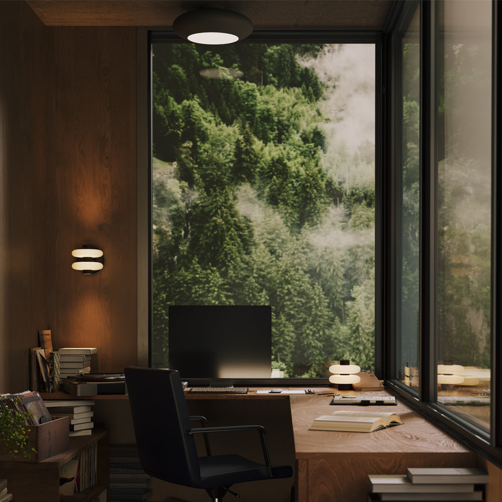 Mise en ambiance du plafonnier allumé au-dessus d'un bureau en bois face à la forêt.