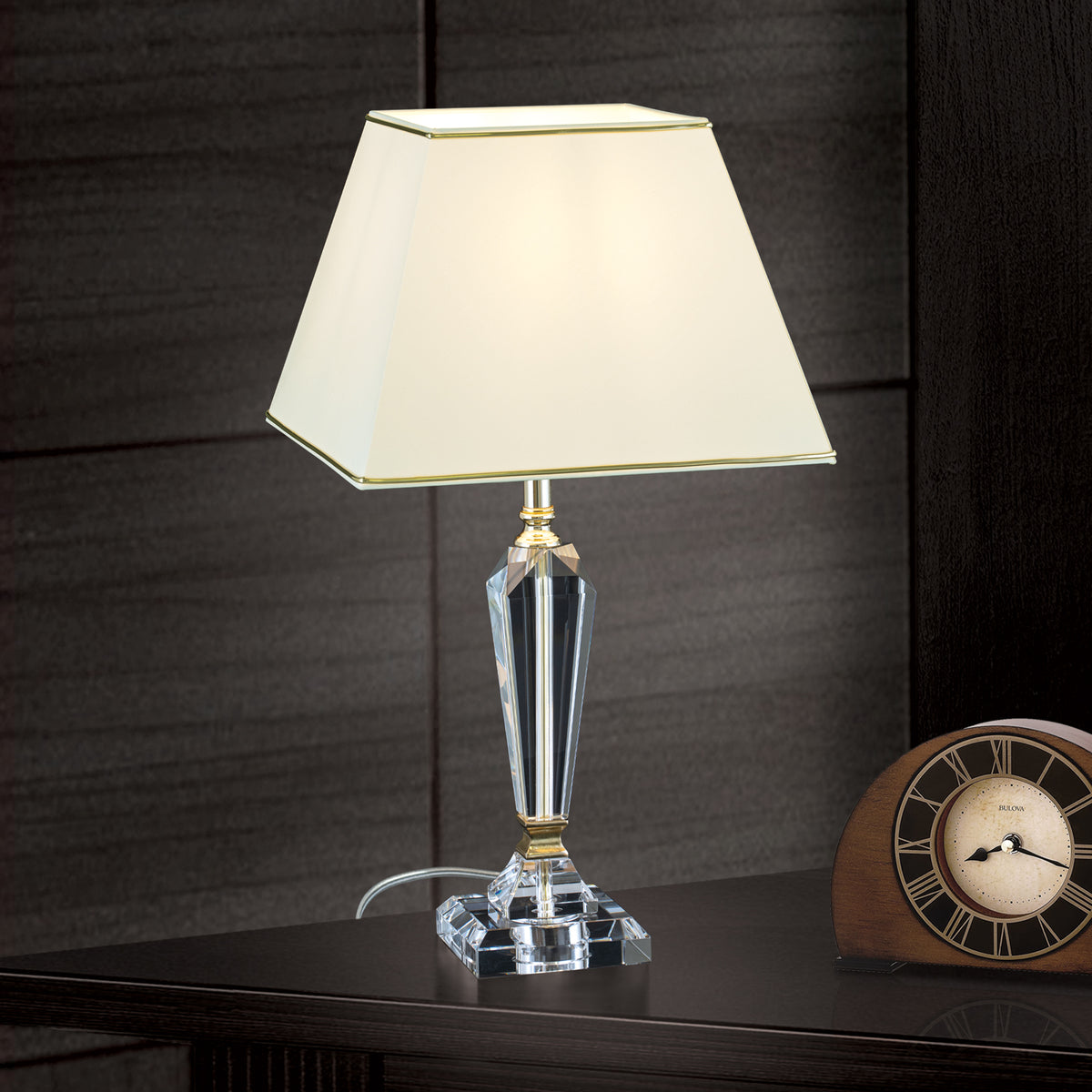 Lampe allumée sur meuble sombre, près d'une pendulette en bois, décor mural noir