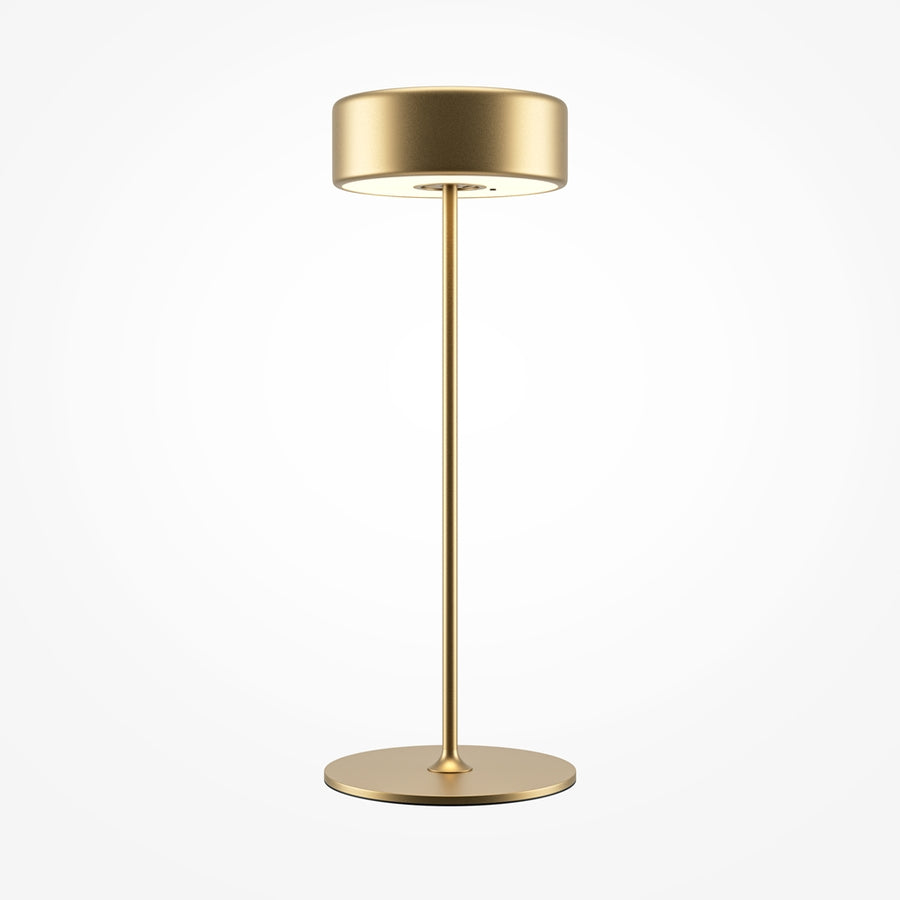 Lampe de table dorée de face sur fond blanc, abat-jour cylindrique et tige fine.