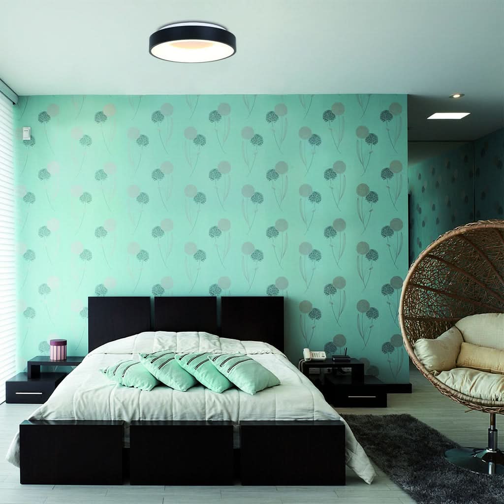 Vue large de la chambre avec plafonnier, fauteuil suspendu en rotin et lit aux coussins menthe.