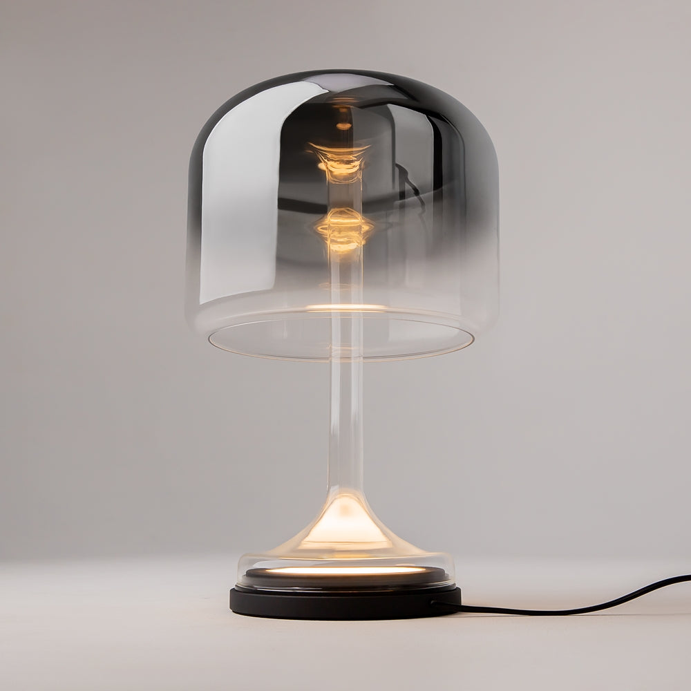 Lampe allumée posée sur une table, halo chaud traversant le verre fumé, câble visible
