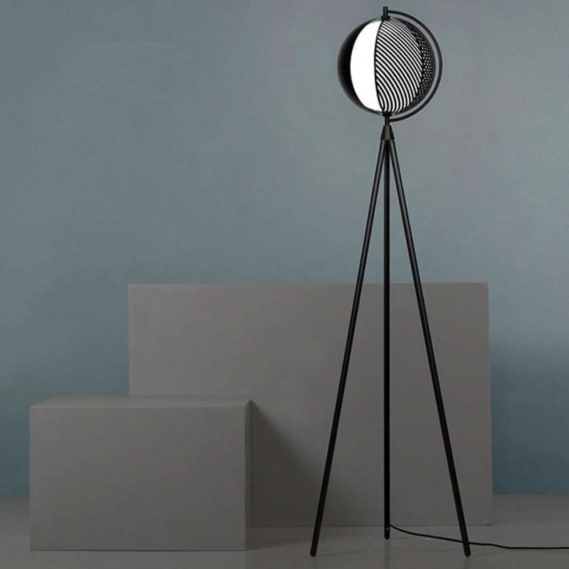 Lampadaire trépied noir posé devant blocs gris, détail du socle et câble