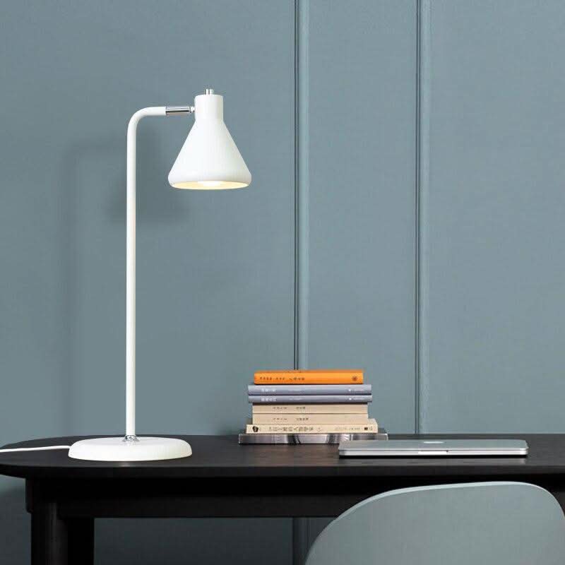 Lampe blanche allumée sur bureau sombre, mur bleu-gris et pile de livres colorés.