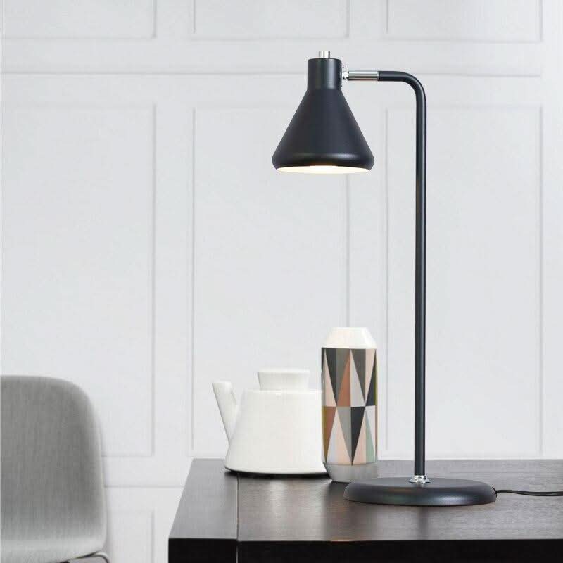 Lampe noire éclairée sur table en bois foncé devant un mur blanc à moulures.