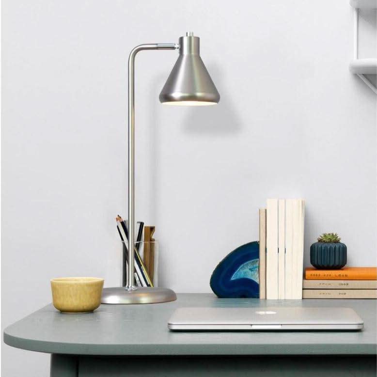 Mise en ambiance bureau : lampe nickel allumée posée près d'un ordinateur portable et de livres.