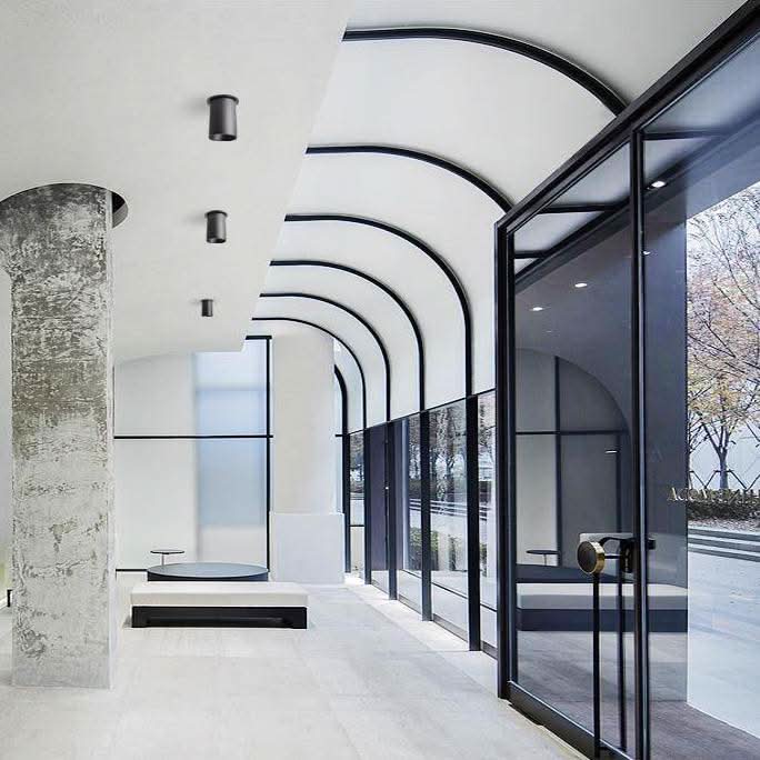 Couloir contemporain avec spots noirs cylindriques au plafond et grandes baies vitrées cintrées.
