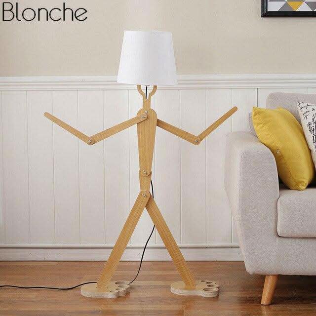 Lampadaire bois dans salon, abat-jour blanc éteint, canapé gris et coussin jaune à droite.