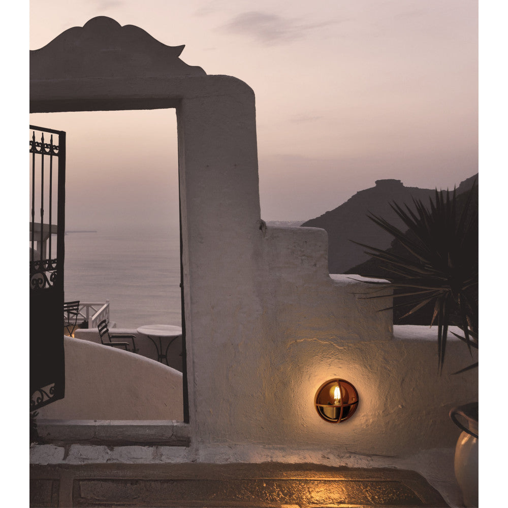 Applique extérieure allumée sur mur blanc crépi, terrasse face à la mer au crépuscule.