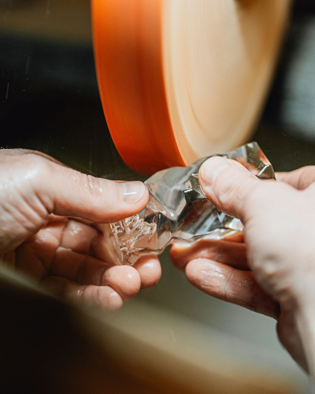 Mains d'artisan polissant un élément de cristal facetté devant une meule orange