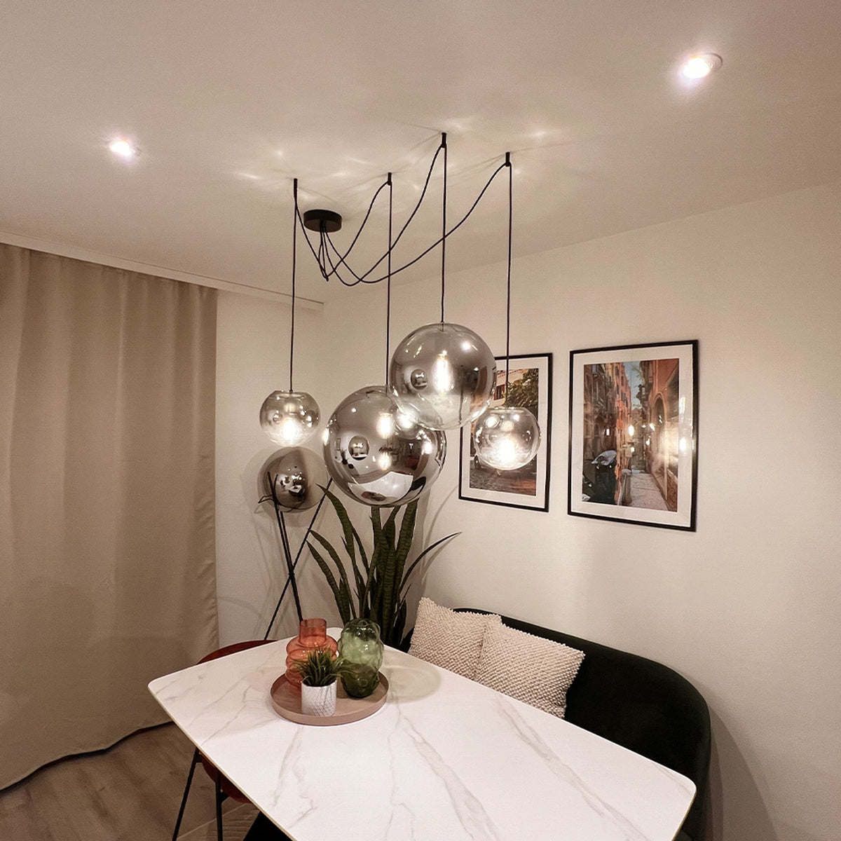 Suspension multiple à globes verre fumé et miroir, câbles noirs au-dessus d'une table.