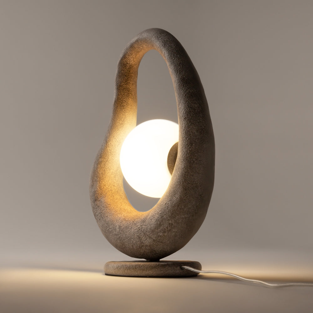Profil du luminaire en matière pierreuse, boule opaline allumée sur socle rond.