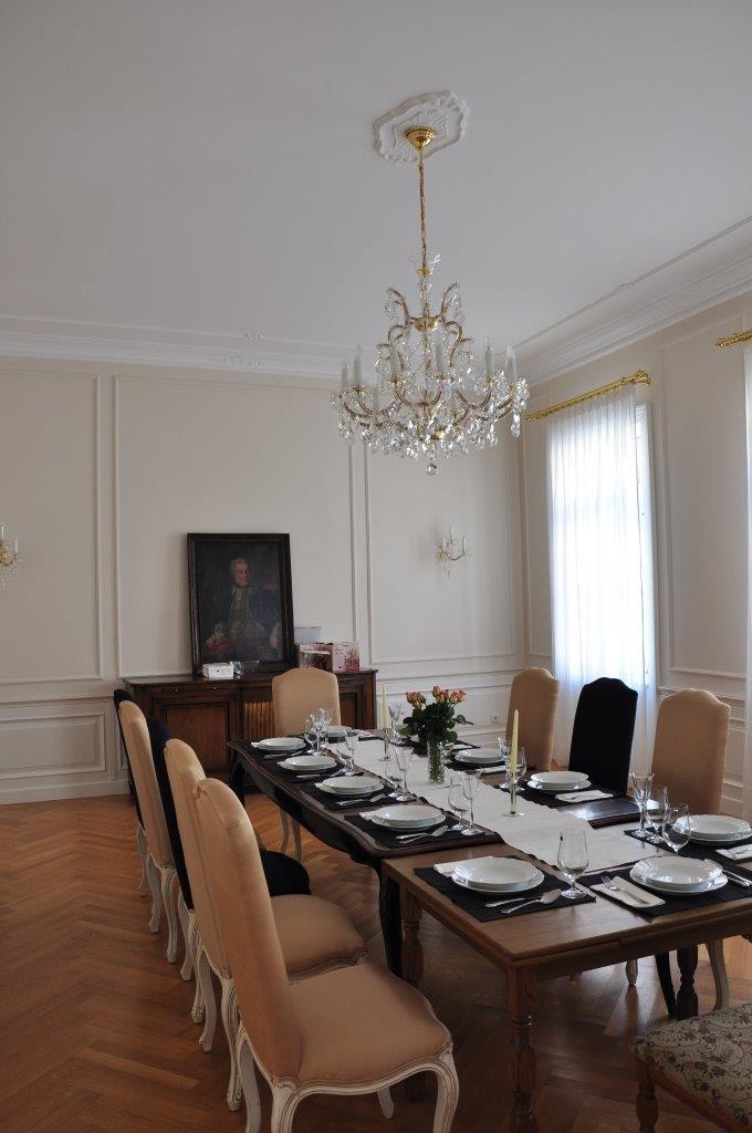 Lustre allumé au-dessus d'une table dressée, plafond mouluré et parquet chevron