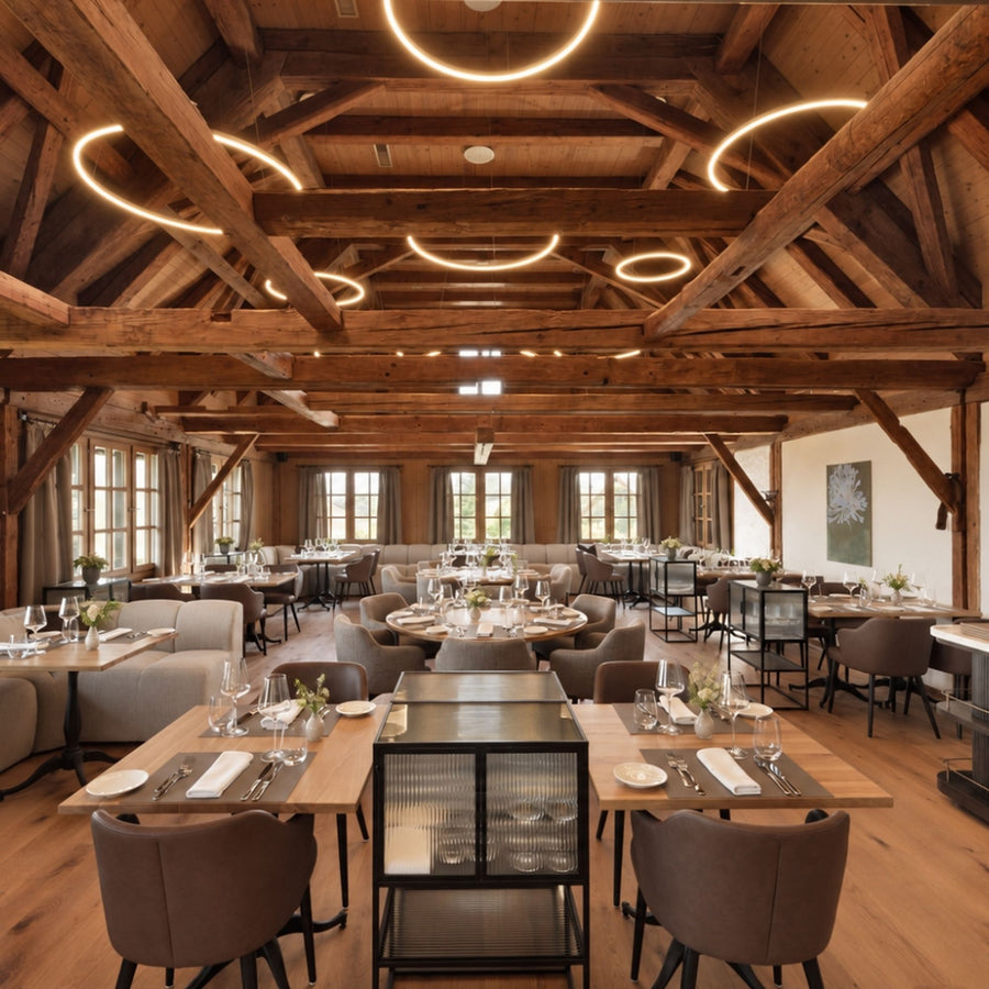 Salle de restaurant en charpente bois éclairée par plusieurs anneaux lumineux suspendus