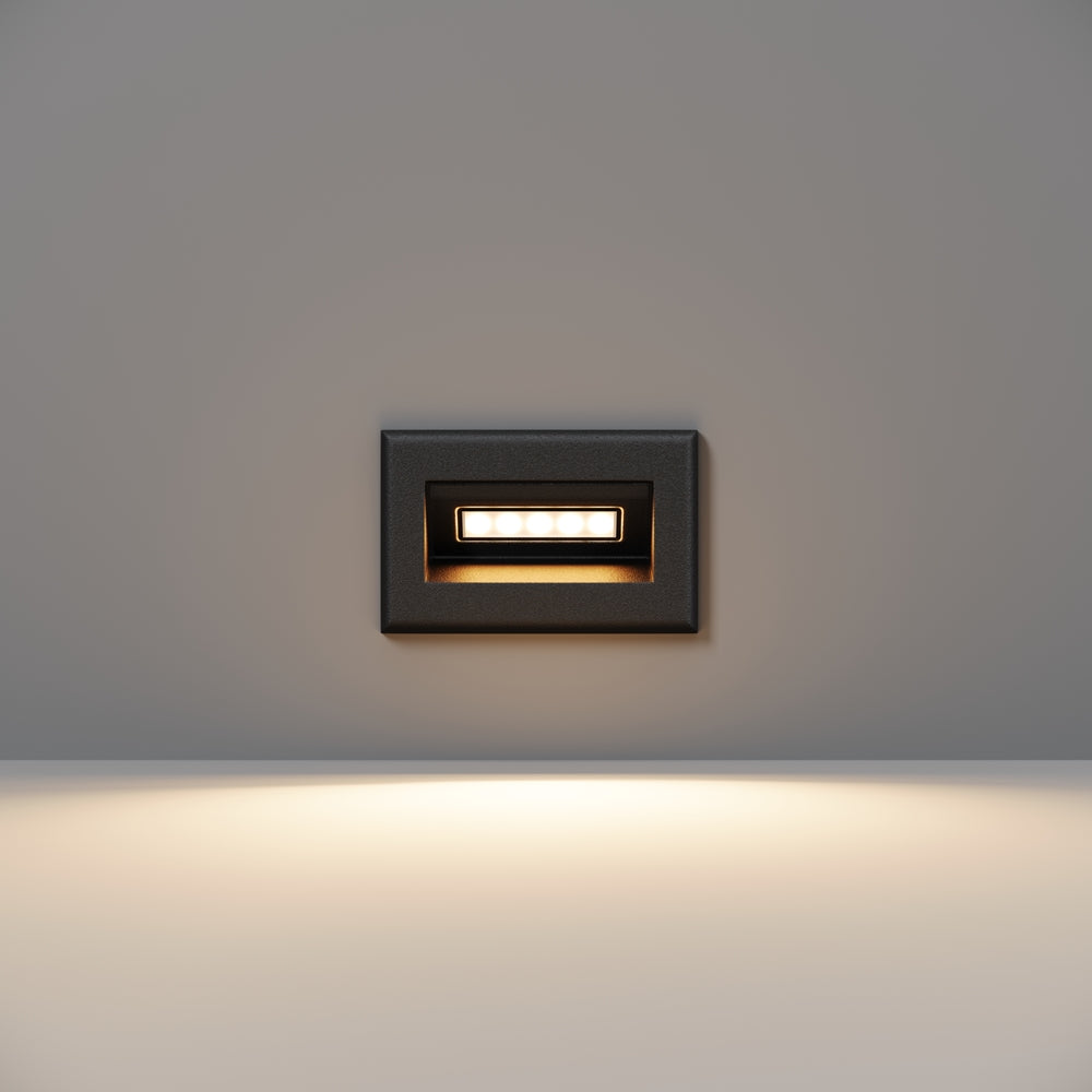 Petit modèle noir encastré dans un mur gris, lumière diffusée vers le bas.