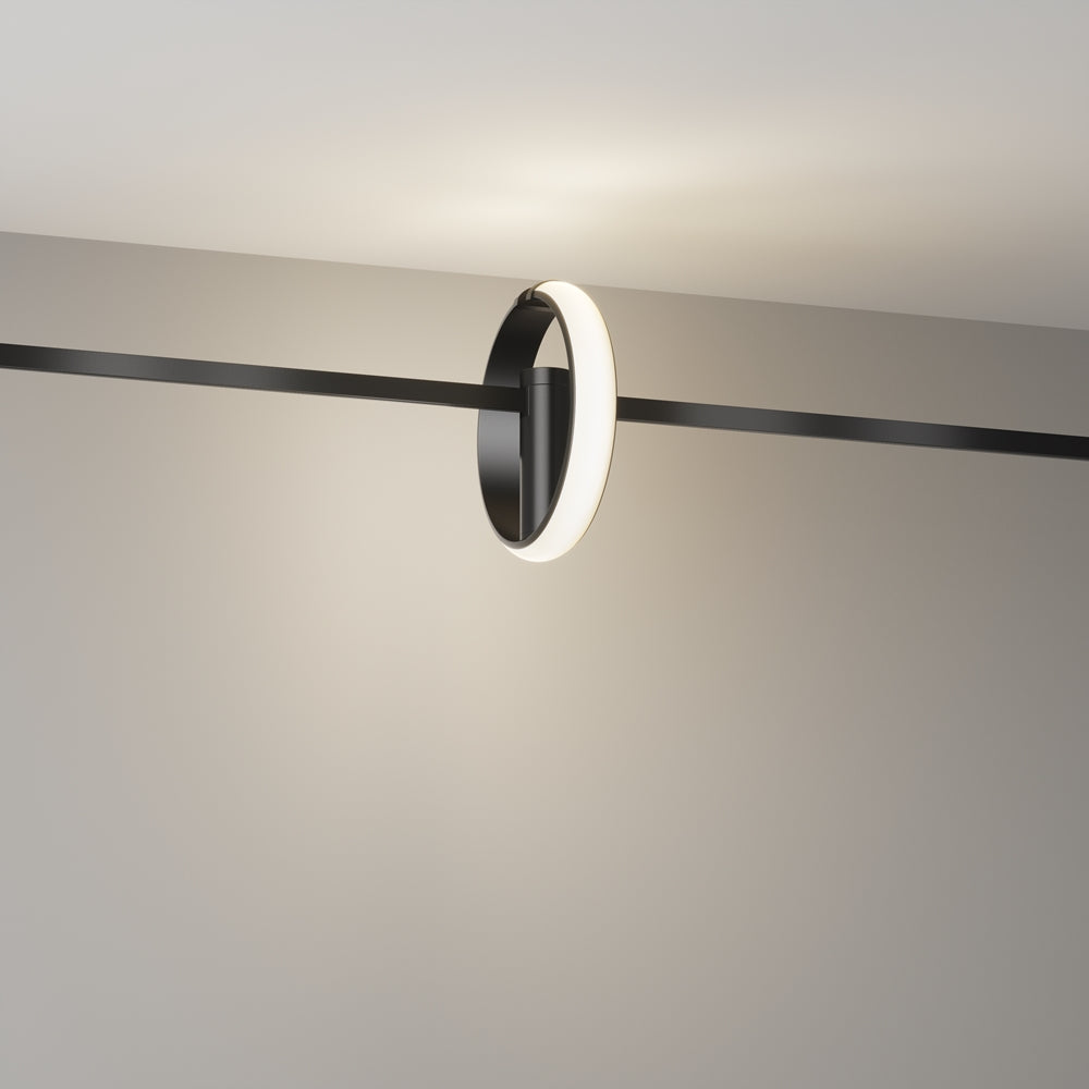 Luminaire suspendu devant un mur clair, halo lumineux diffus autour de l'anneau